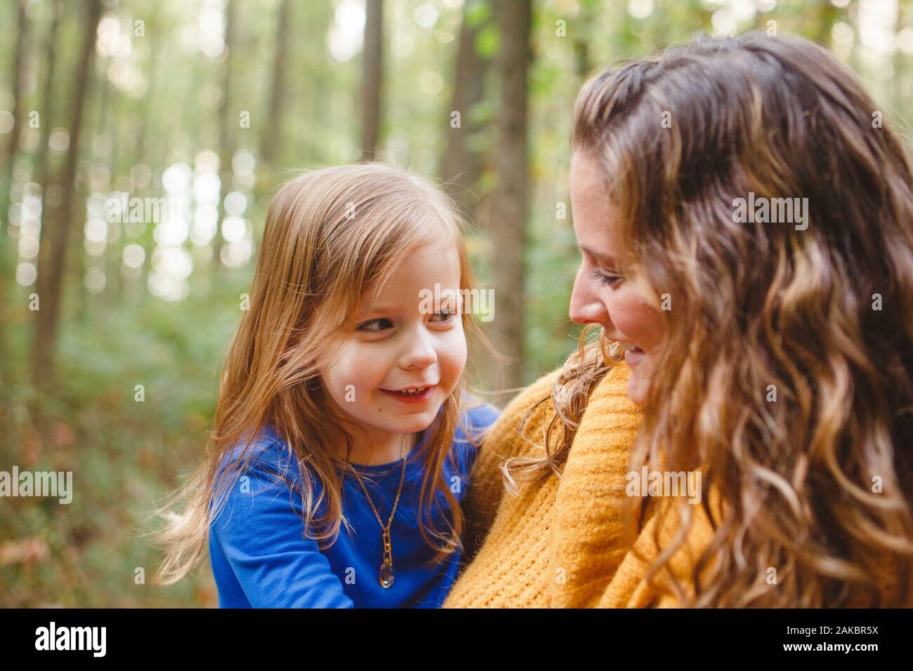 Ein kleines Mädchen schmiegt sich in die Arme ihrer Mutter, während sie zusammen lächeln Stockfoto