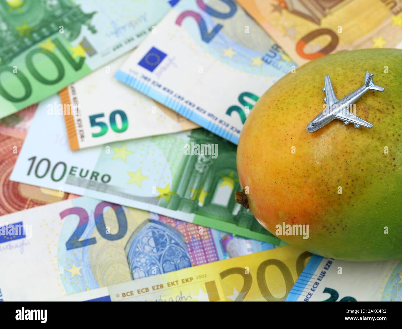 Miniatur Flugzeug auf Mango mit Euro-banknoten auf Hintergrund, Konzept der Kosten für exotische Früchte importieren Stockfoto