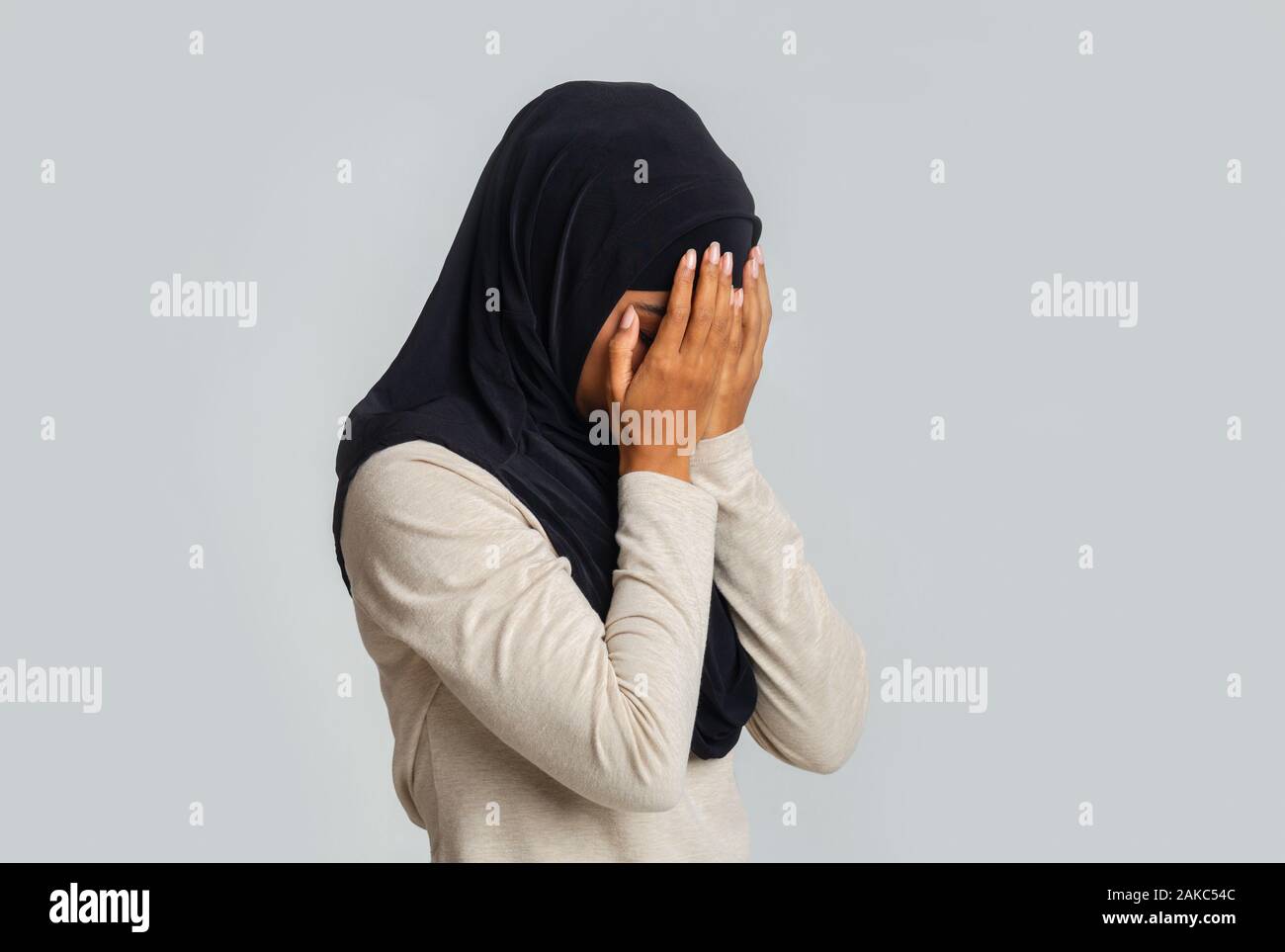 Gewalt gegen Muslime Konzept. Verärgert schwarze Frau im hijab für Gesicht, Hände, über grauer Hintergrund weinen, freier Speicherplatz Stockfoto