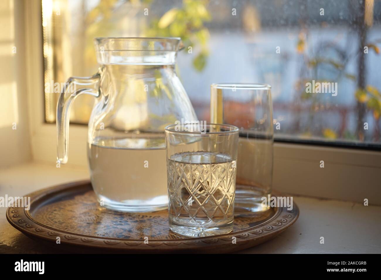 Ein Krug Wasser und zwei Gläser in einem Fach auf der Fensterbank. Stockfoto