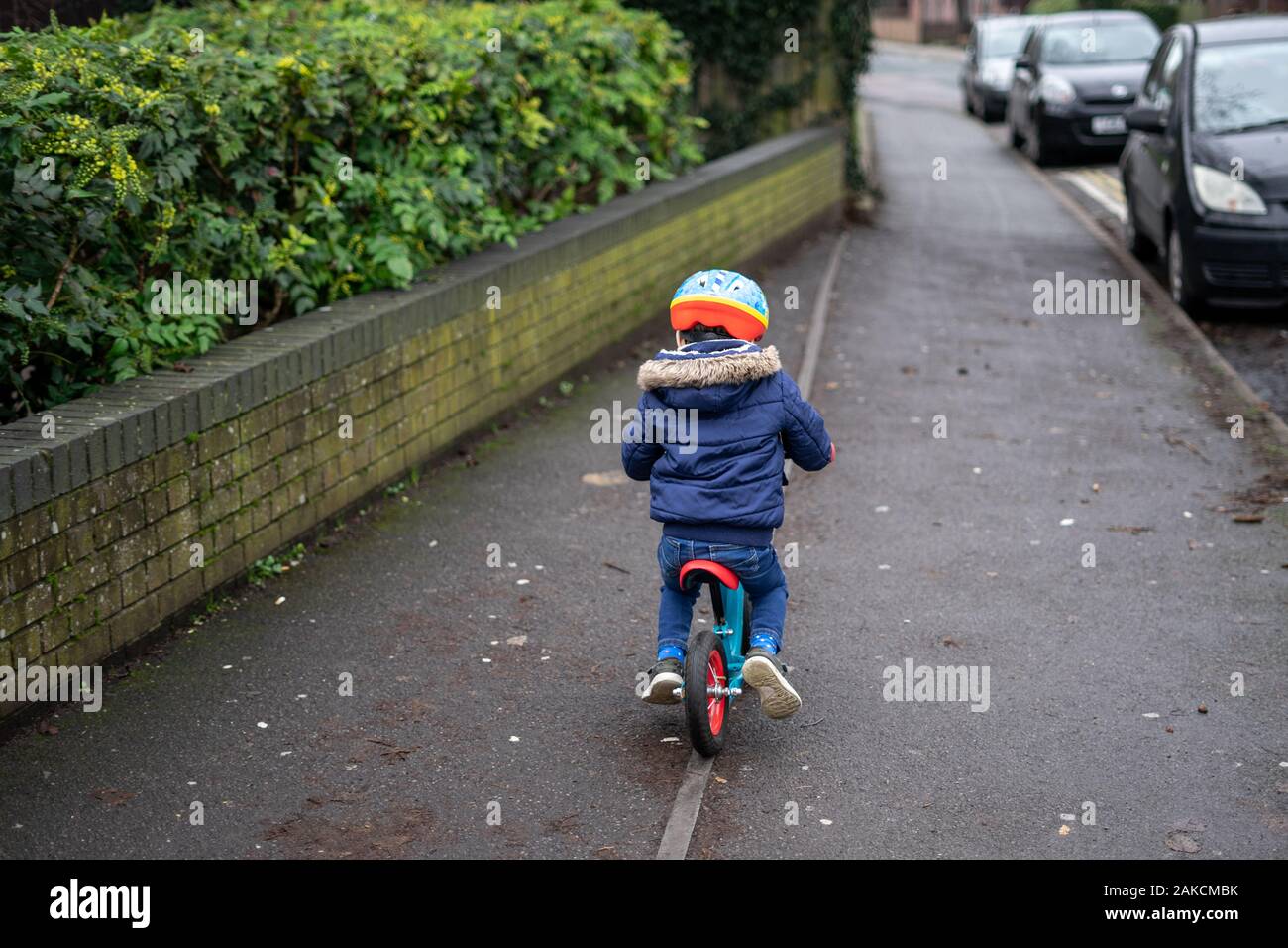 Ein kleiner Junge, der mit seinem Fahrrad auf dem Straßenbelag unterwegs ist und einen Fahrradhelm trägt Stockfoto