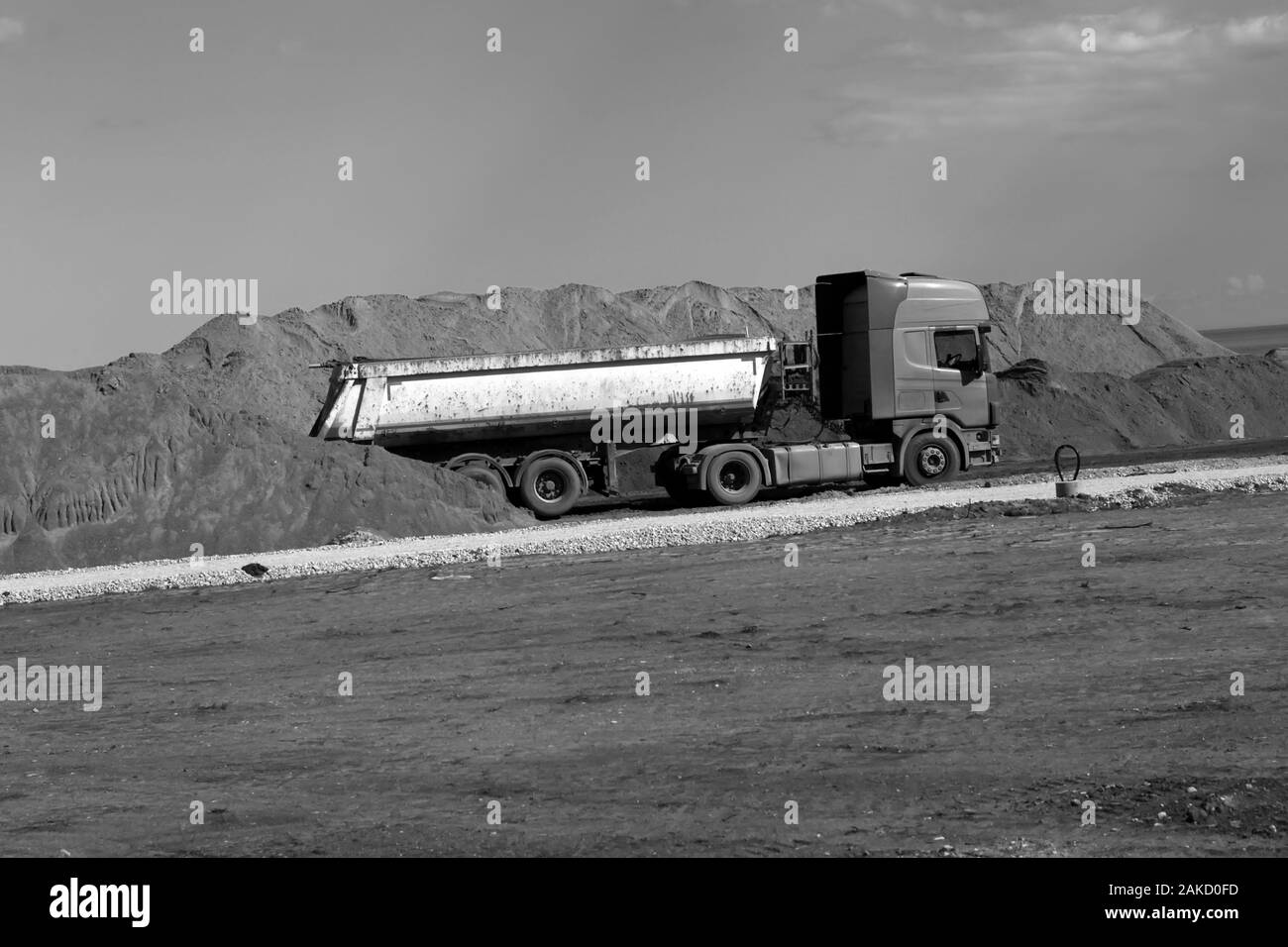 Schwarz-weiß Bild von alten Lastwagen in der Nähe von Sand Haufen an der Straße Baustelle. Große alte roadworking Kipper bis Klettern bau Konzept Stockfoto
