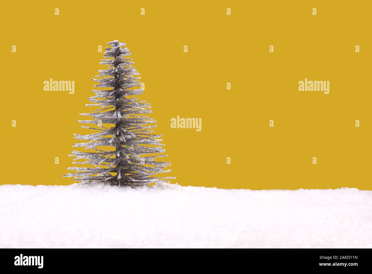 Spielzeug silber Weihnachtsbaum auf künstlichen weißen Schnee vor gelbem Hintergrund Stockfoto