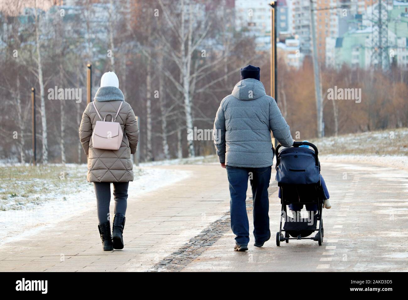 Paar mit einem Baby Stroller Walking im Winter Park während der. Schneewetter, Konzept der Mutterschaft, Eltern mit Kinderwagen Stockfoto