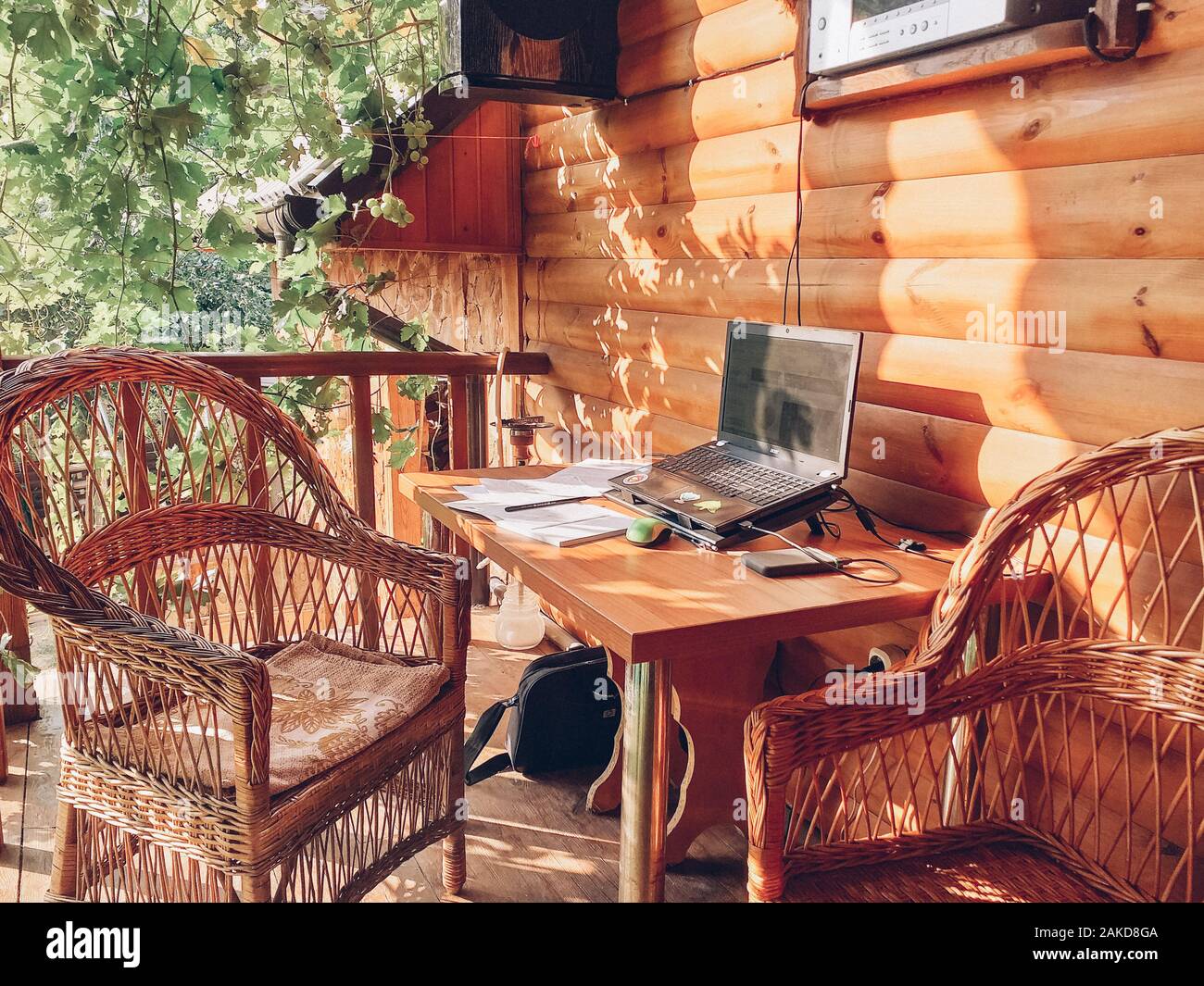 Arbeitsplatz in einem offenen Bereich im Garten mit Korbmöbeln unter der Trauben. Ein Ort für Freiberufler. Das Konzept der freien Arbeit. Stockfoto