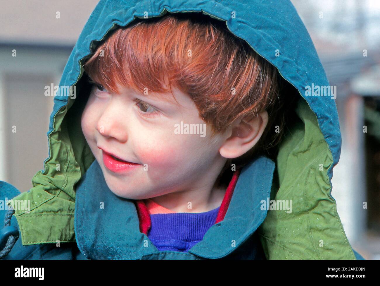 Junge rothaarige Junge in einer Regenjacke während ein leichter Regen oder Nieselregen wetter Veranstaltung lächeln Stockfoto