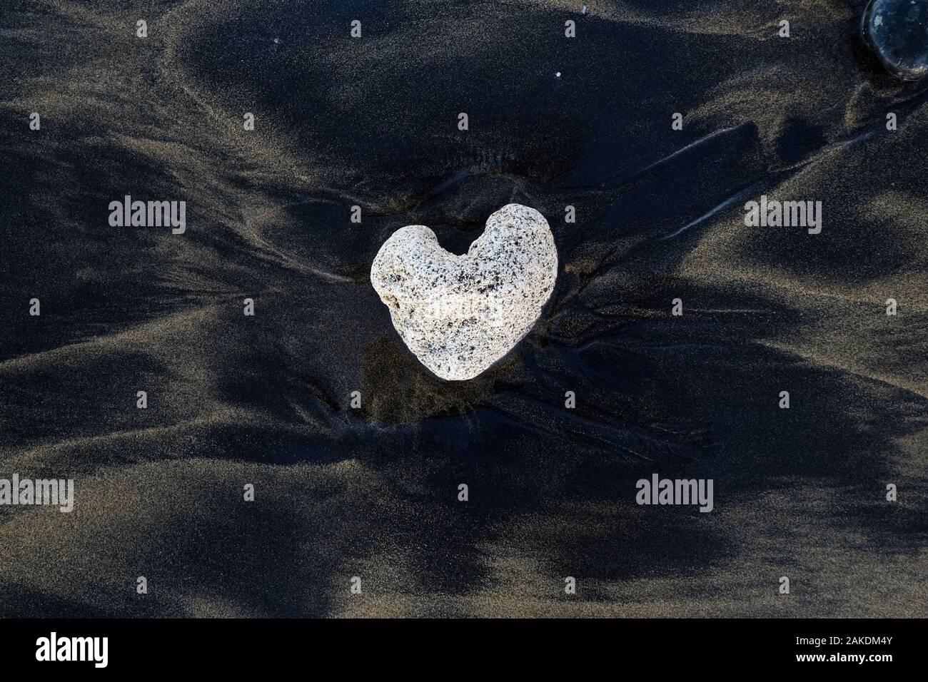 Weißen herzförmigen Stein auf schwarzen vulkanischen Sand. Stockfoto