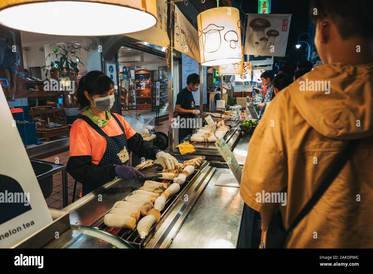 Eine Frau grillt an einem Lebensmittelstand im Shi Lin Night Market, Taipei, Taiwan, für eine Schlange von Kunden die Pilze aus der Austernzucht Stockfoto