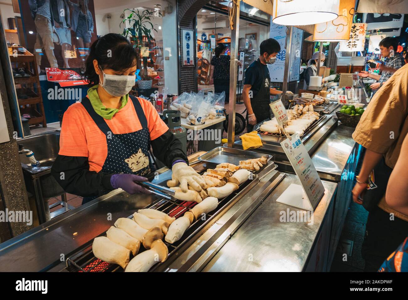 Eine Frau grillt an einem Lebensmittelstand im Shi Lin Night Market, Taipei, Taiwan, für eine Schlange von Kunden die Pilze aus der Austernzucht Stockfoto