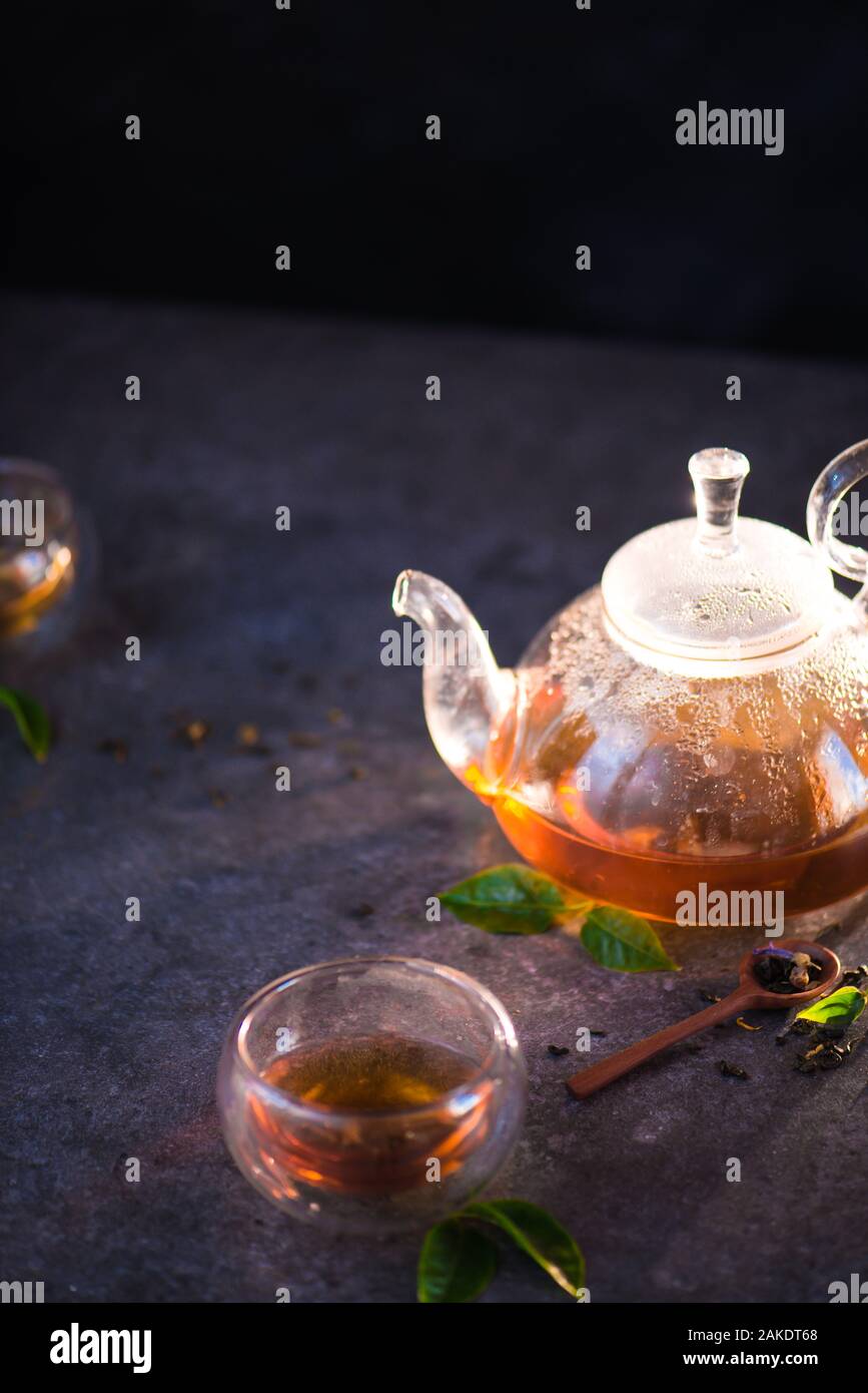 Teekanne aus Glas mit Doppelwand Glas Schalen auf einem Stein Hintergrund mit Tee Blätter Stockfoto