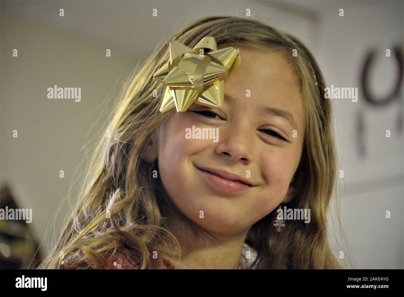 7 Jahre altes Mädchen zur Weihnachtszeit mit echten Geschenken, einige für sie, einige mit Schleife in den Haaren und einem Baum im Hintergrund Stockfoto