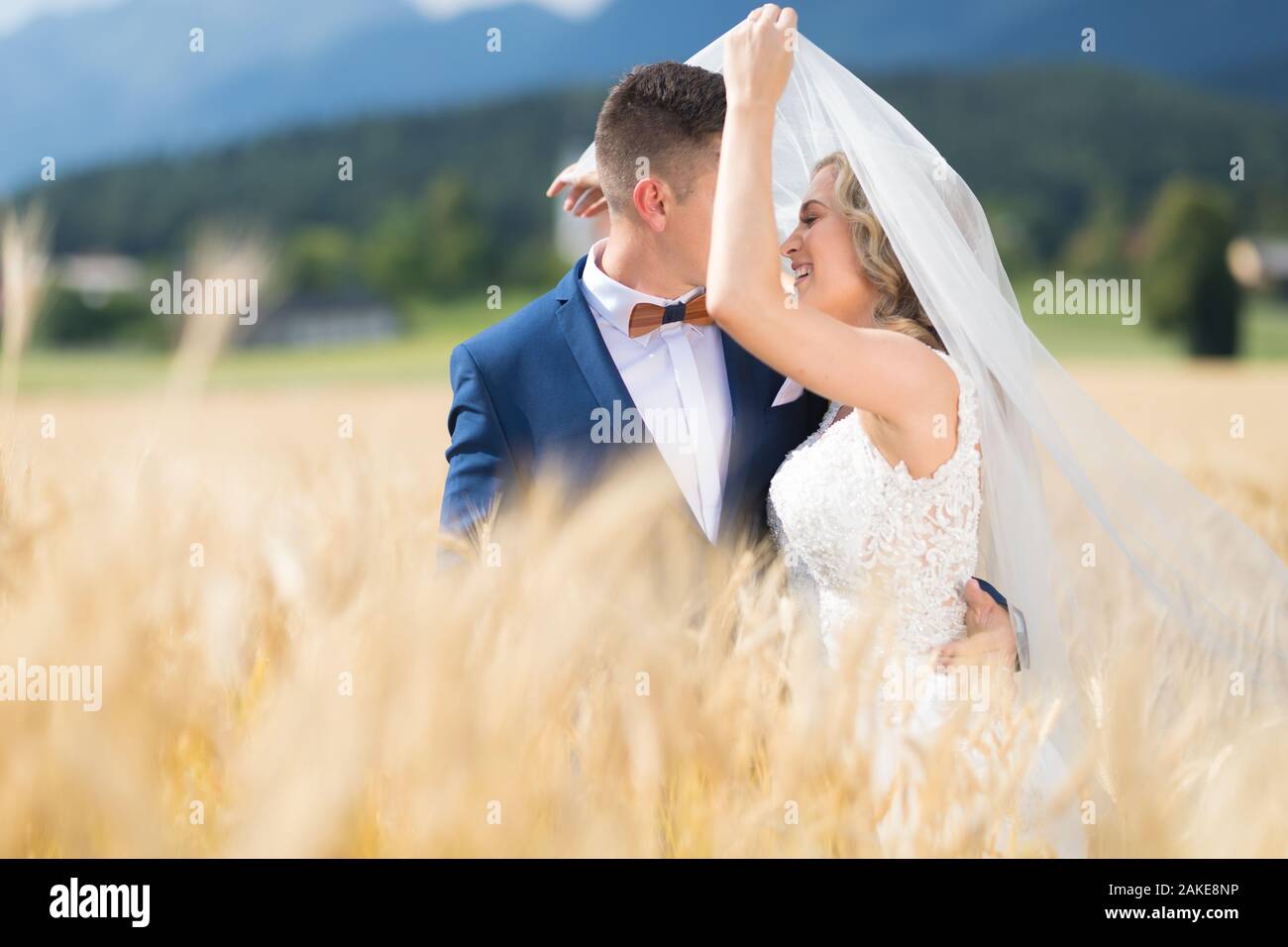 Bräutigam Braut zärtlich umarmt, während der Wind bläst, ihren Schleier in Weizen Feld irgendwo in der slowenischen Landschaft. Stockfoto