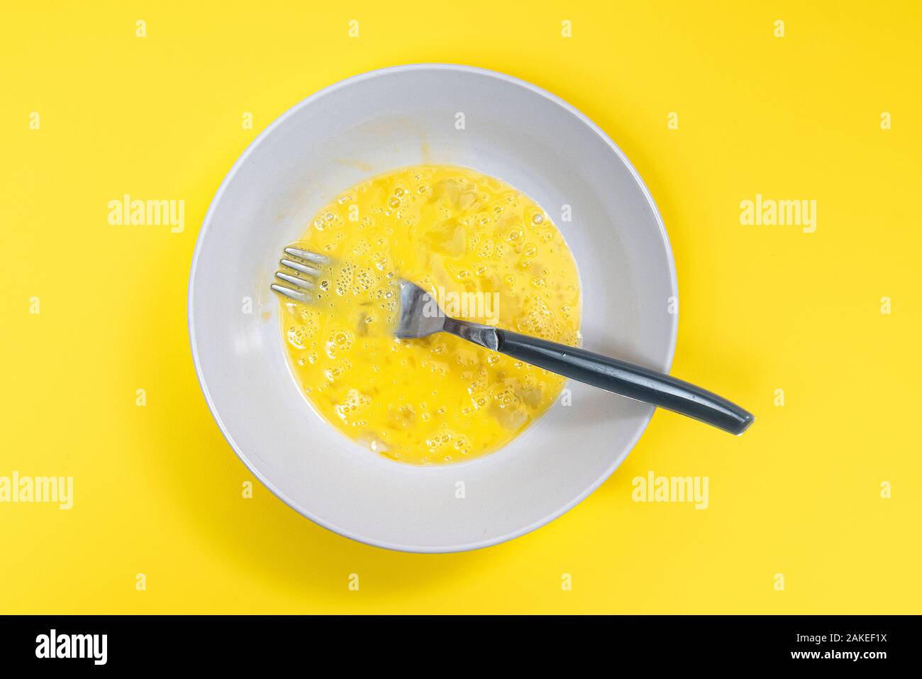 Ein geschlagenes Ei auf der Platte bereit auf einem gelben Oberfläche gekocht zu werden Stockfoto