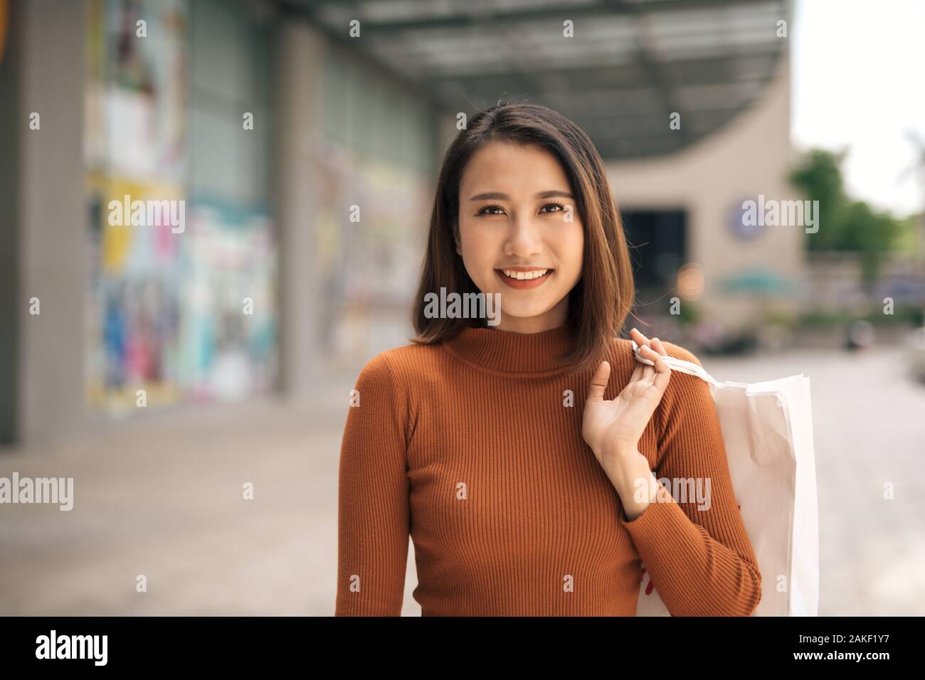 Portrait von fröhlichen jungen asiatischen Frau mit Einkaufstüten an Outdoor Mall Stockfoto