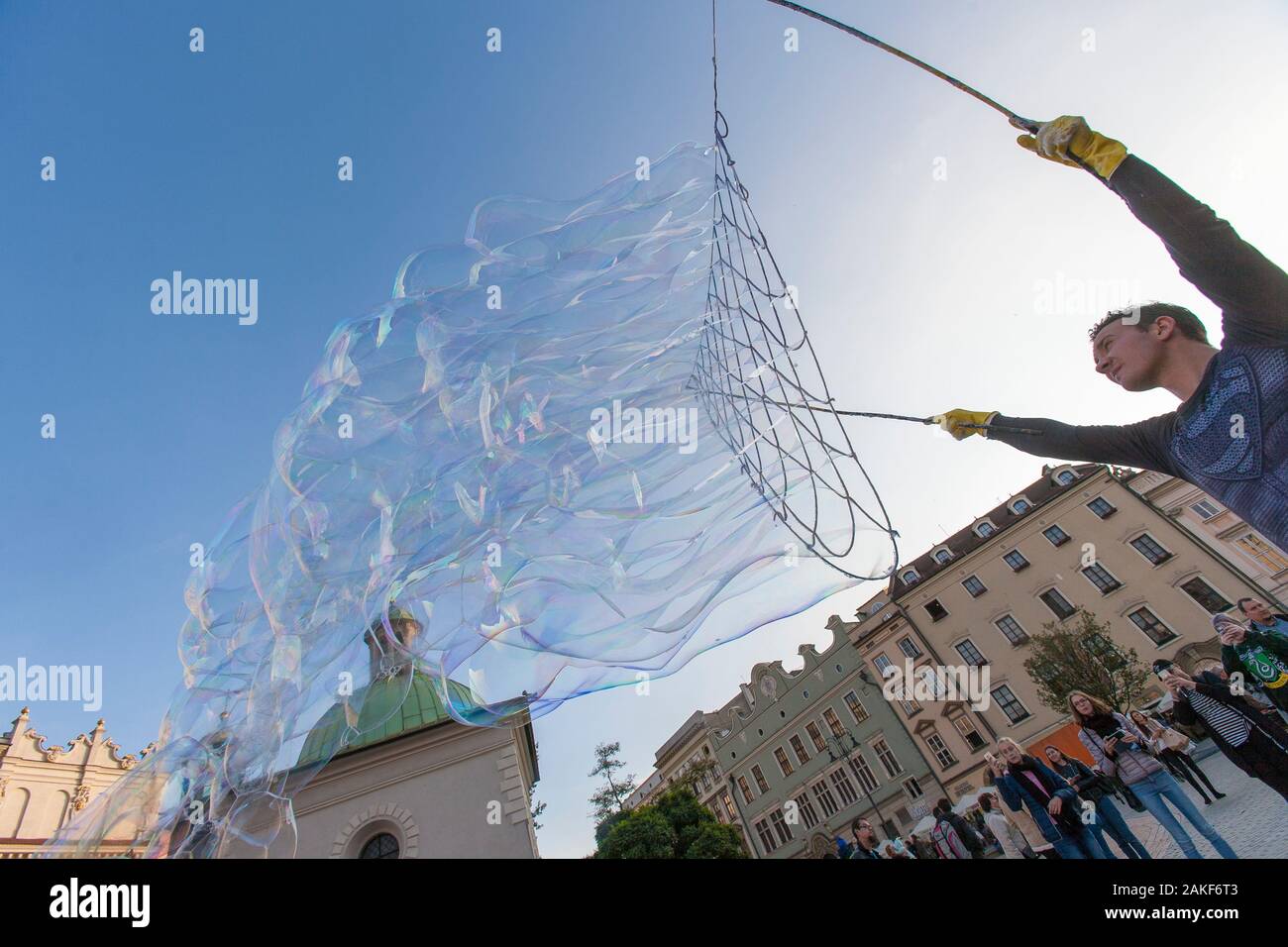 Die Menschen beobachten, wie ein Mann im Rynek Glowny (Hauptmarktplatz) im Zentrum von Krakow (Krakow), Polen, riesige Blasen erzeugt Stockfoto
