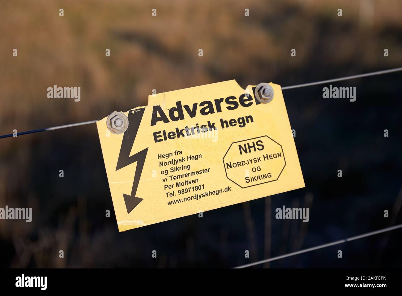 "Advarsel-Elektrisk hegn' (Warnung - Electric Fence'), Zeichen, die in dänischer, verschraubt mit Kabel (NHS, Nordjysk Hegn Sikring og) Stockfoto