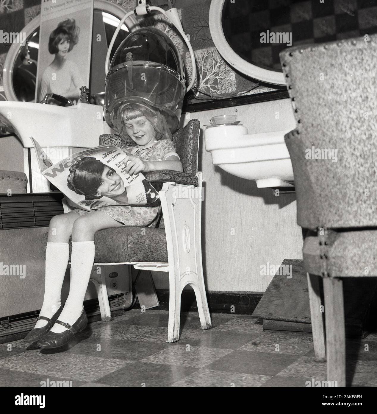 1960, historische, ein junges Mädchen in einem Erwachsenen Damen Friseur, in einem Stuhl Lesen der Frau Zeitschrift, England, Großbritannien sitzen. Stockfoto