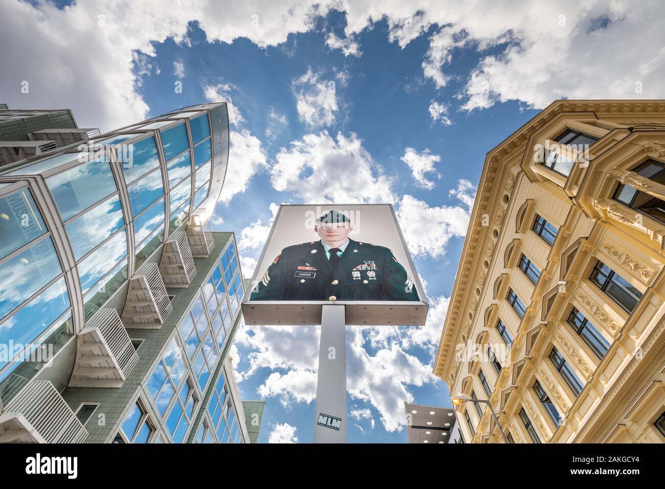 Weitwinkelansicht von unten am Checkpoint Charlie in Berlin, mit dem Bild des amerikanischen Soldaten in der Mitte, gegen eine blaue Sommerwolkenlandschaft Stockfoto