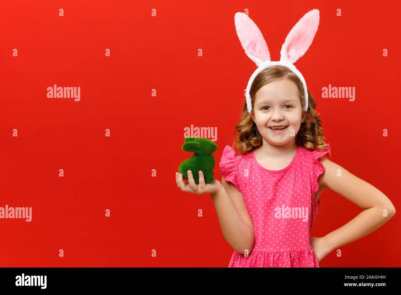 Frohe Ostern. Süße kleine Mädchen im bunny Ohren hält eine grüne Kaninchen. Closeup Baby auf einem roten Hintergrund. Stockfoto