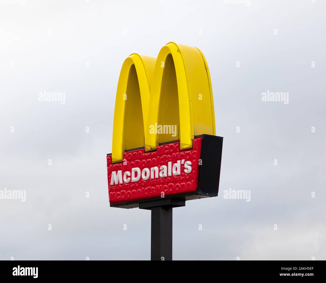 Junction One Retail Park, Rugby, Warwickshire, Großbritannien: McDonalds Restaurantschild an einem schwarzen Pfosten gegen einen hellgrauen Himmel. Stockfoto