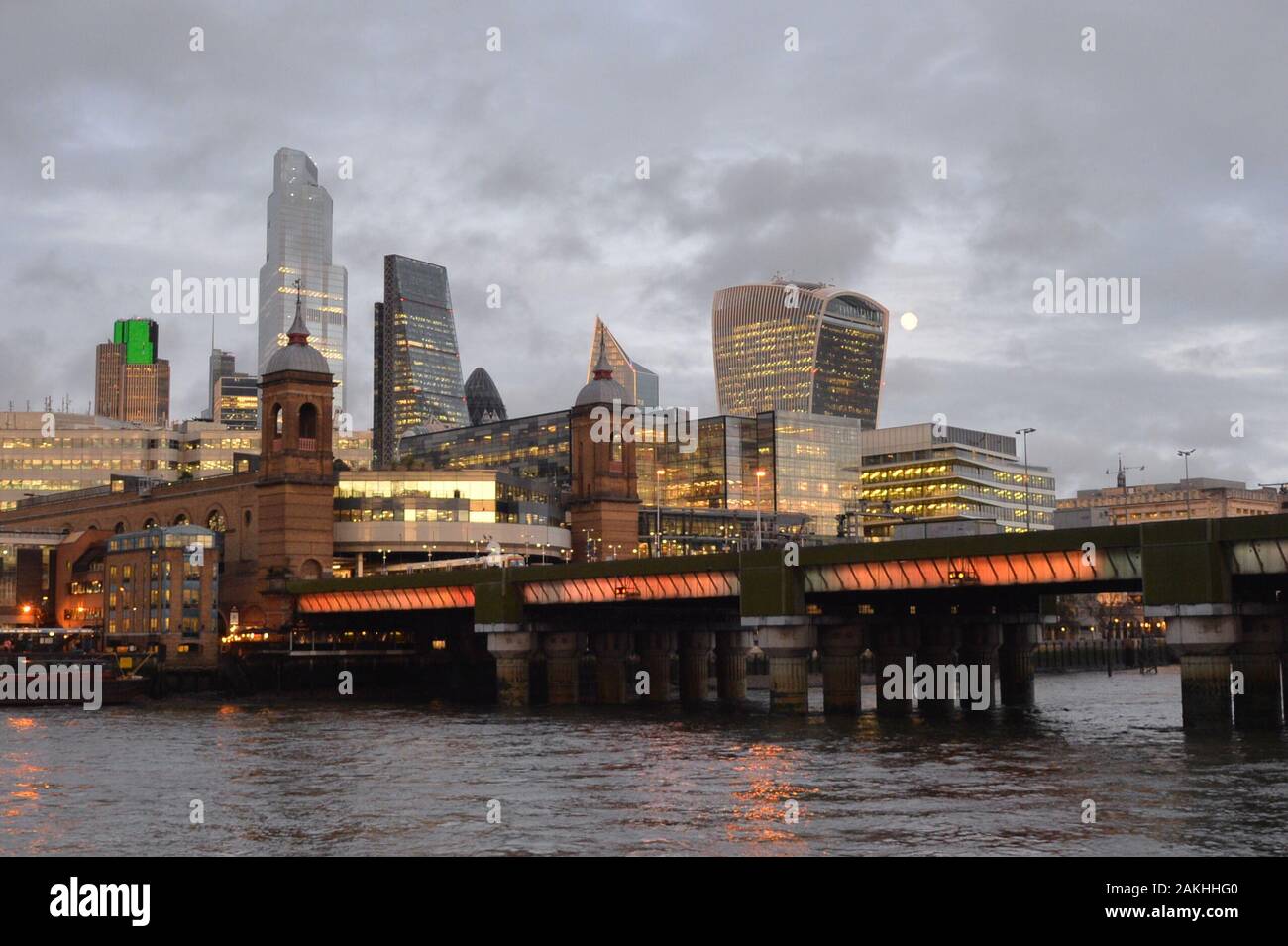 Skyline von London City und Eisenbahnbrücke Cannon Street im nassen Winter am späten Nachmittag mit Mond und Lichtern in Büroblöcken. Stockfoto