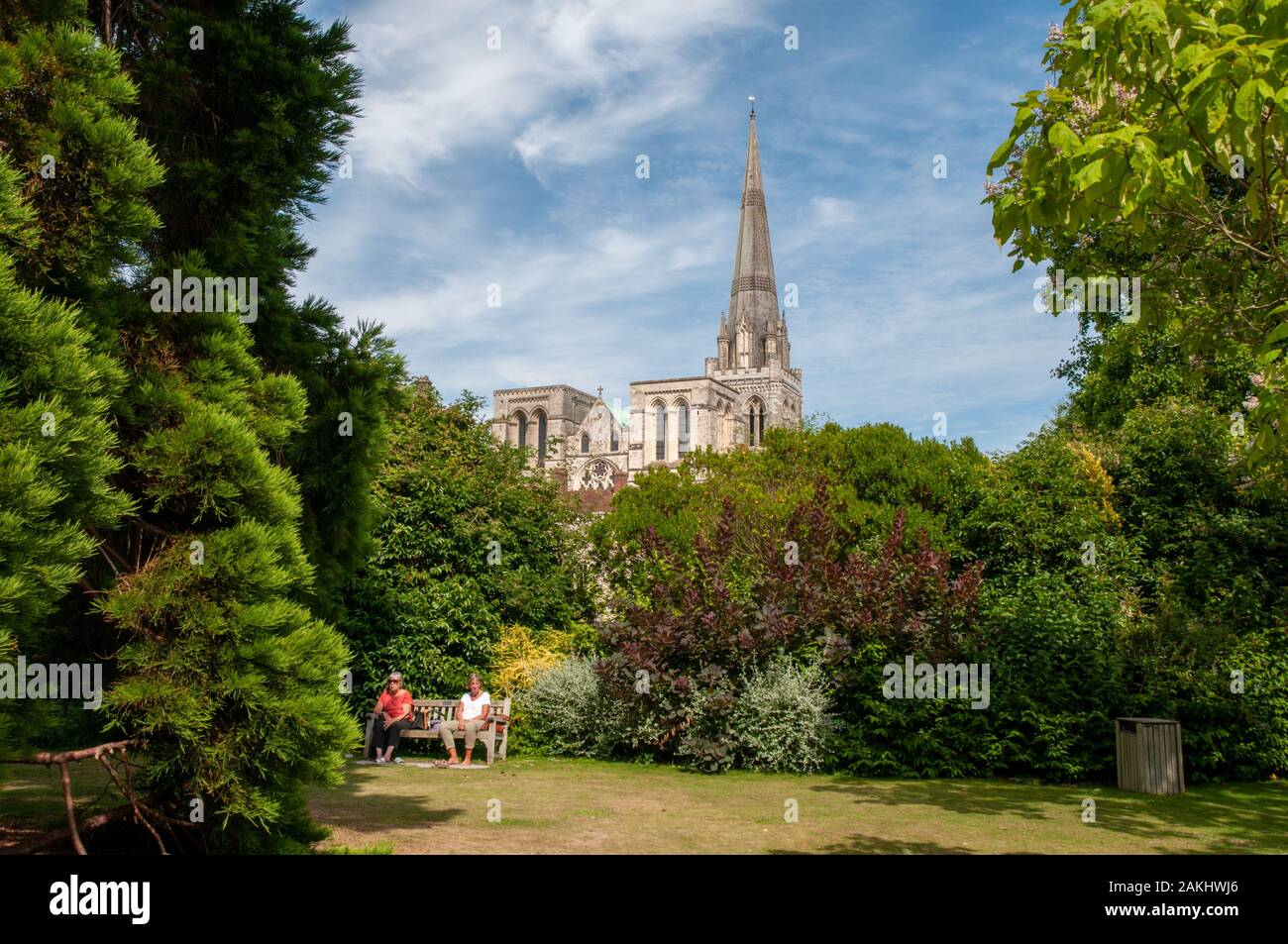 Zwei Frauen entspannen auf einer Bank im Bishop's Palace Gardens mit der Kathedrale von Chichester, West Sussex, als Hintergrund. Stockfoto