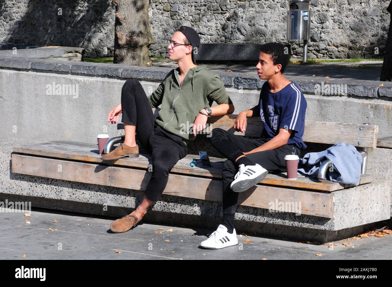 Zwei junge Männer, die sich in der Sonne auf einer öffentlichen Bank entspannen, Kilkenny. Mit Permissionl. Stockfoto