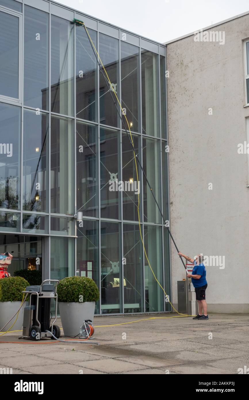 Fensterreinigung mit dem Reinigungspol REACH und Waschfenster an einem dreigeschossigen Glaseingang zu einem Büroblock in Schweinfurt, Bayern, Deutschland. Stockfoto