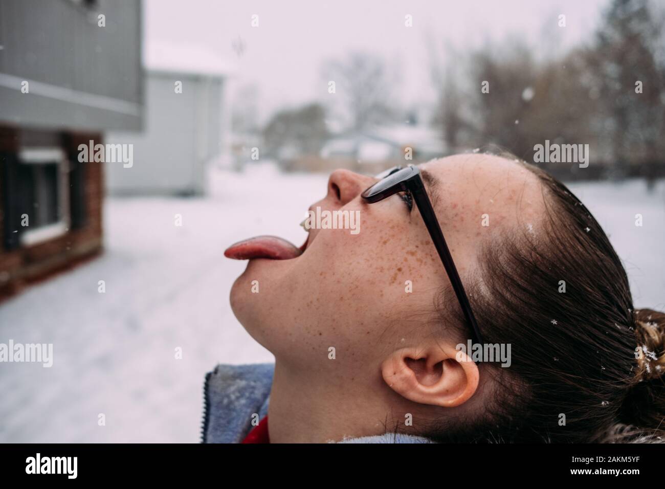 Seitenansicht eines Mädchens mit Brille, die Schneeflocken mit Zunge fängt Stockfoto