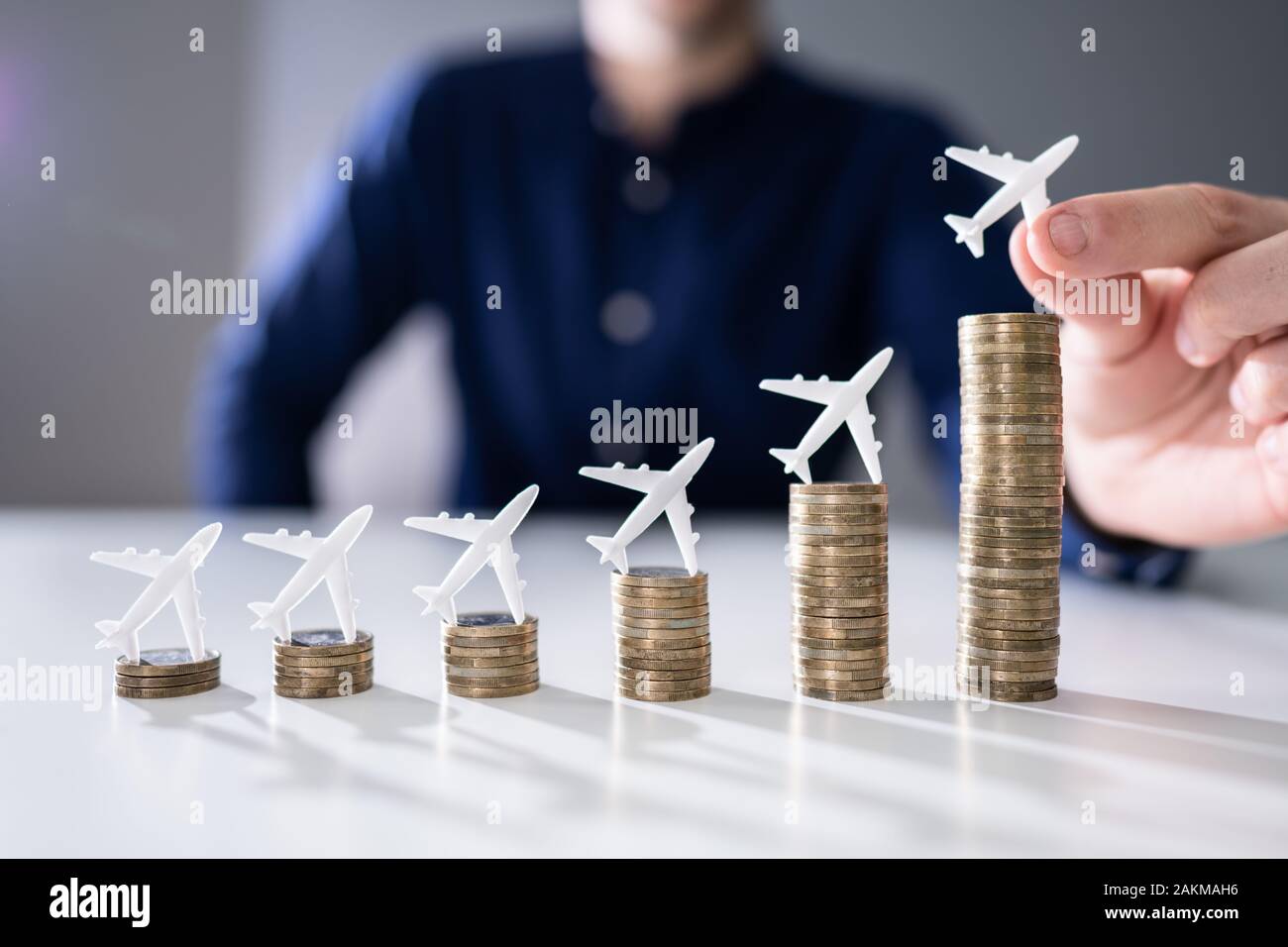 Nahaufnahme einer menschlichen Hand kleinen Flugzeug auf zunehmende Gestapelte Münzen über Schreibtisch Stockfoto