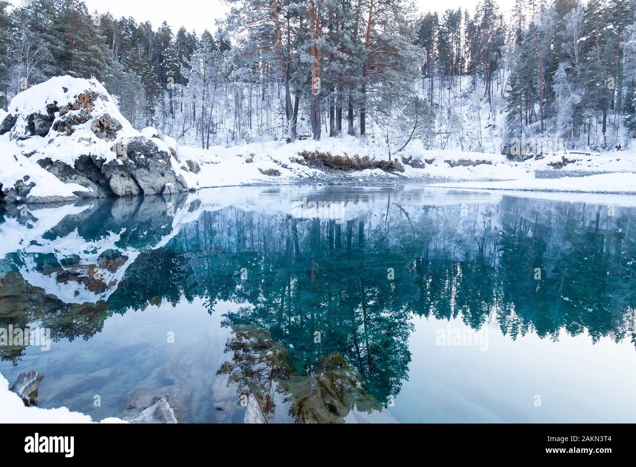 Sehenswürdigkeiten in den Bergen des Altai, blaue Seen nicht Einfrieren im Winter um Steine mit grünem Schlamm bedeckt mit Schnee, in denen Bäume und Himmel sind refle Stockfoto