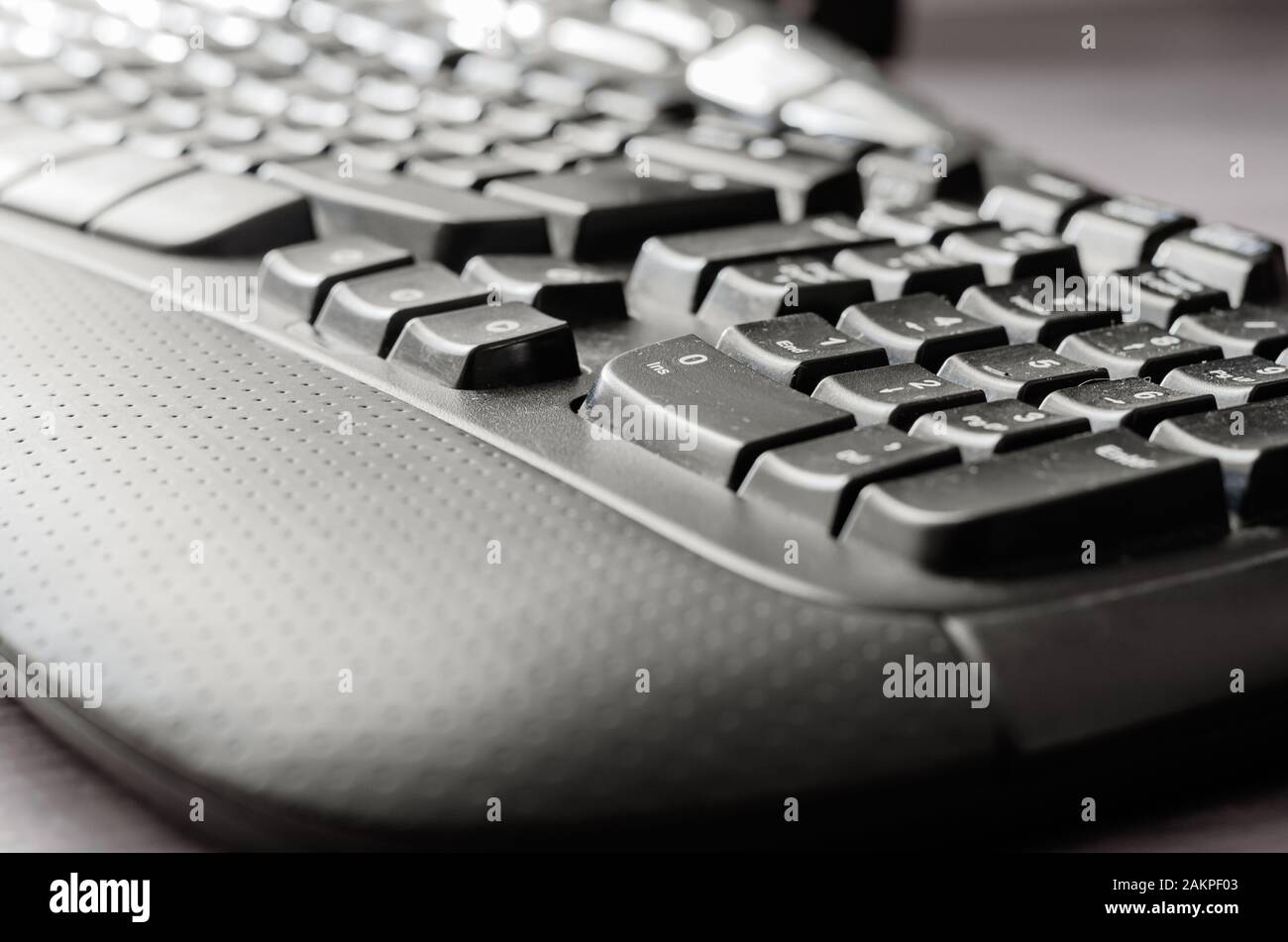 Nahaufnahme einer dunkel gestürzten Computertastatur. Schwarze ergonomische Tastatur auf einem hellgrauen Schreibtisch. Aufnahmen auf Augenhöhe. Selektiver Fokus. Stockfoto