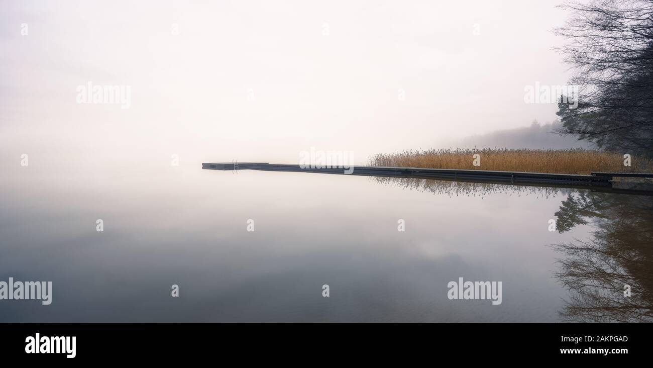 Nebellandschaft mit ruhigem See und Holzsteg am ruhigen Herbstmorgen in Finnland Stockfoto