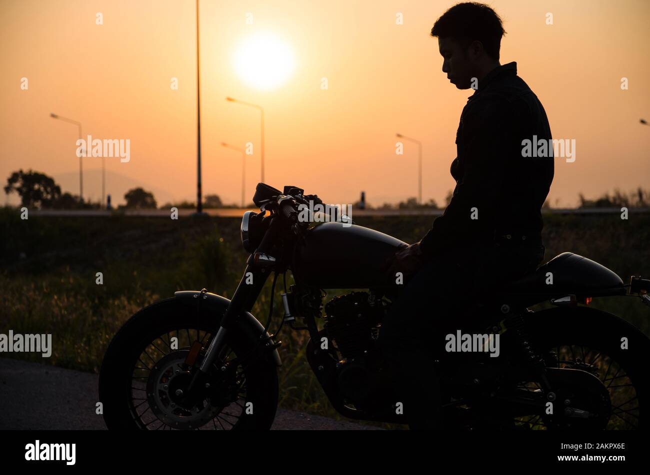 Silhouette eines Mannes, der im klassischen Motorradcafé im Racer-Stil in der Sonnenuntergangsszene unterwegs ist Stockfoto