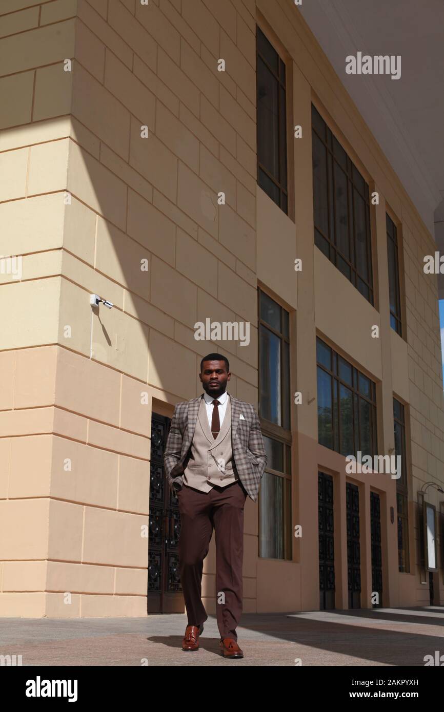 Ganzkörperporträt des afroamerikanischen Models für Männer, das auf die Kamera zuläuft und braunen Anzug trägt. Stilvoller, teurer Business-Look Stockfoto