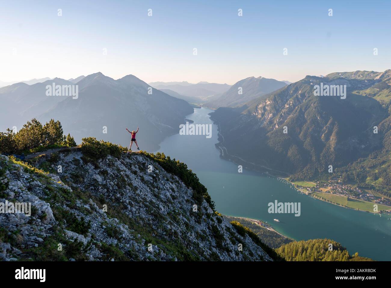 Junge Frau springt in die Luft, Aussicht vom Berg Baerenkopf zum Achensee, links Seebergspitze und Seekarspitze, rechts Rofangebirge Stockfoto