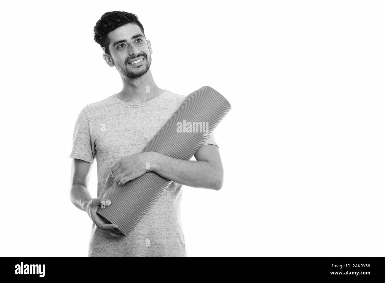 Studio shot der Jungen glücklich Persischen Mann lächelnd, während sie Yoga Matte und Denken Stockfoto