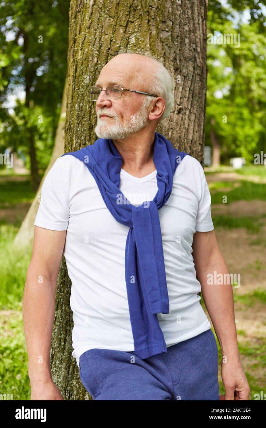 Senior mit Brille lehnt sich gegen Baum im Garten im Sommer Stockfoto
