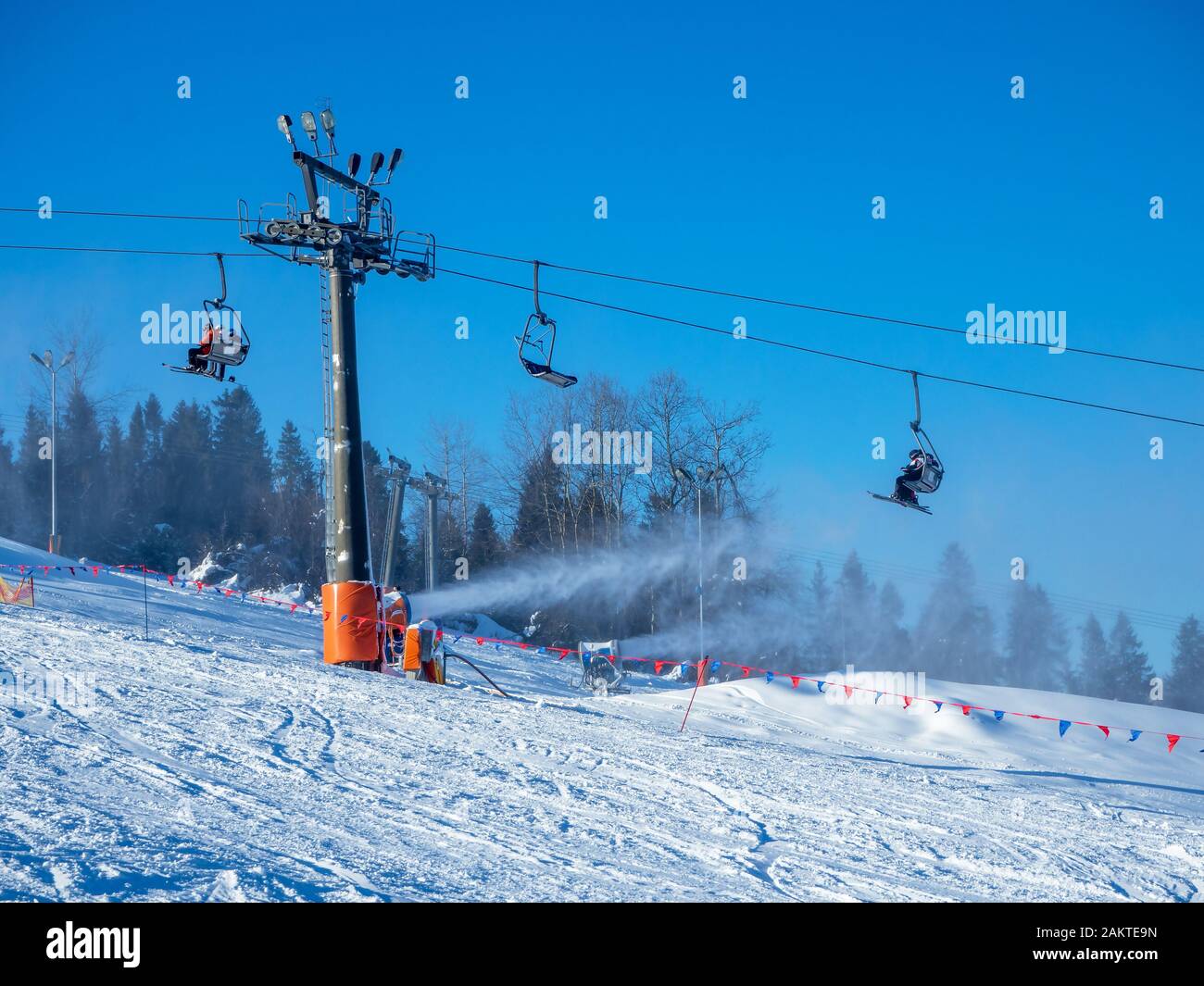 Skilift (Sesselbahn) mit nicht erkennbaren Skifahrern, Skipisten und Schneekanonen in Aktion im Skigebiet Bialka Tahrzanska in Polen Stockfoto