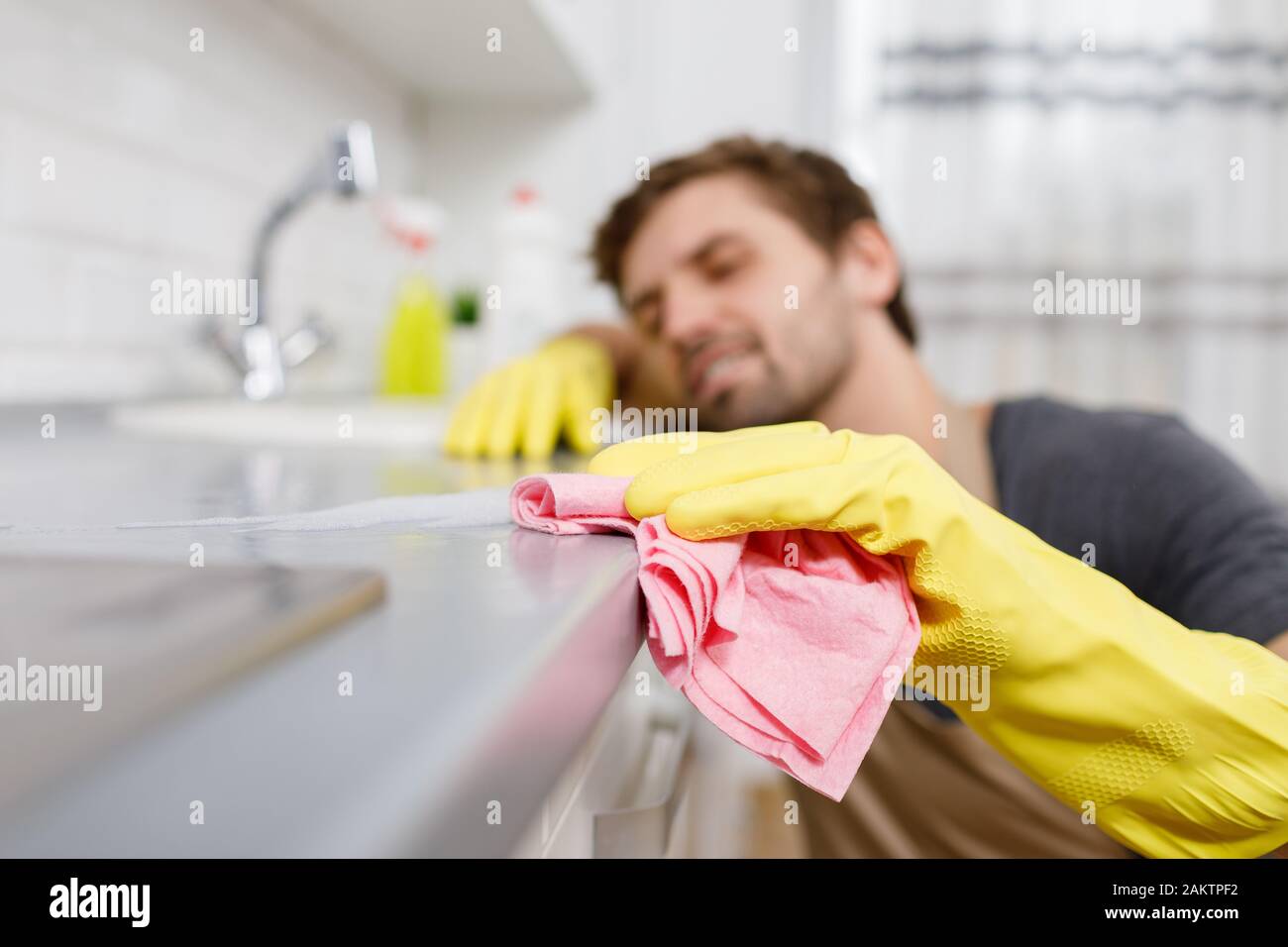 Nahaufnahme des jungen Lasters in gelben Handschuhen, der den Küchentisch mit einem Staubwedel abwischt Stockfoto