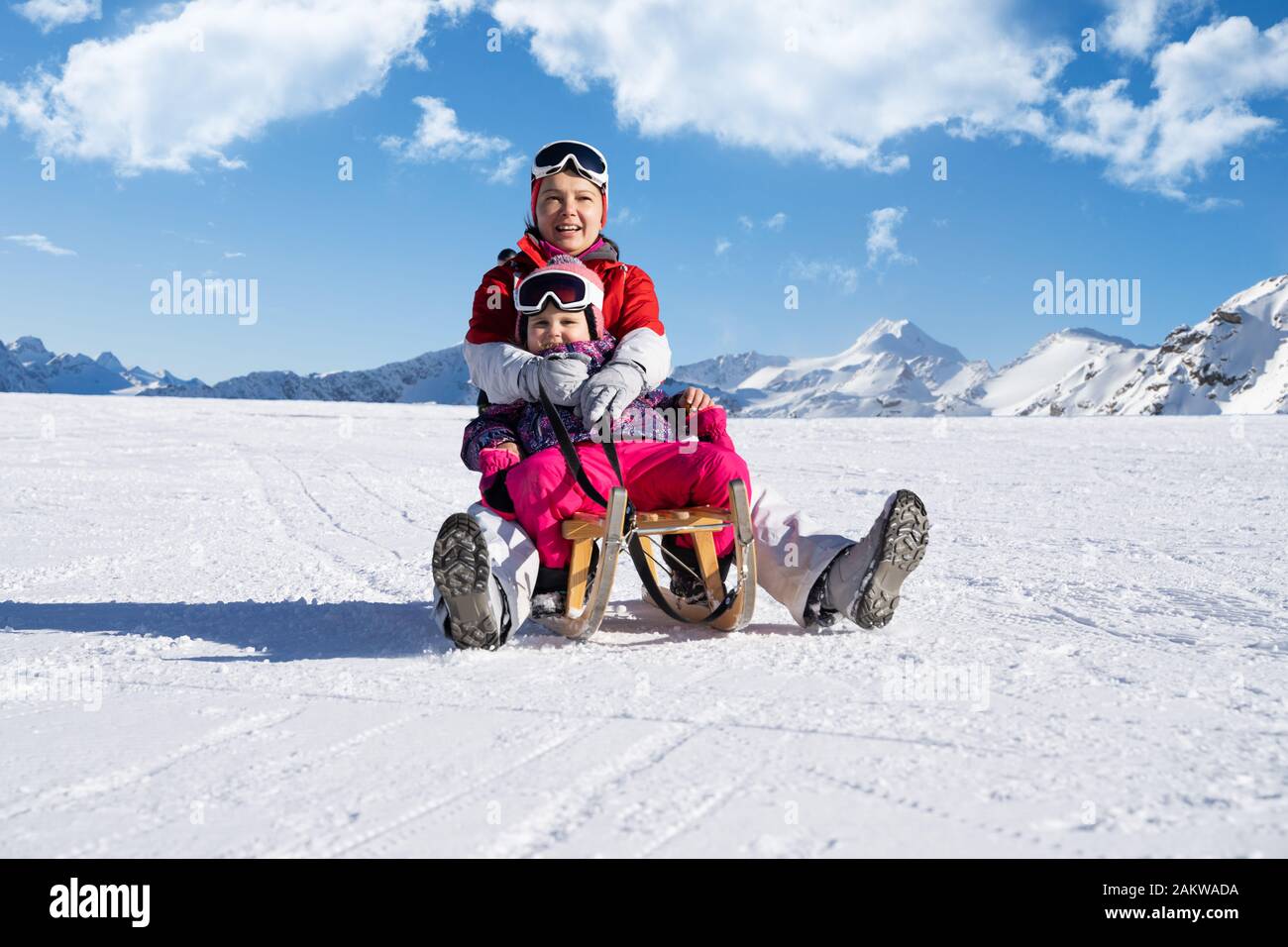 Junge glückliche Mutter und Ihrem kleinen Kind Tochter genießen eine Schlittenfahrt Im Winter Park Stockfoto