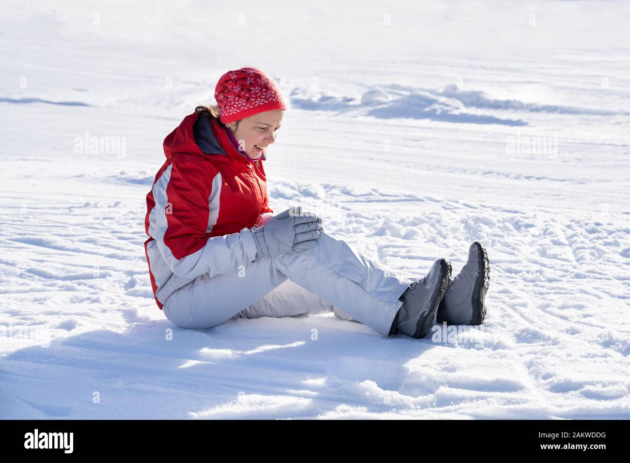 Schöne junge Frau trägt Wollmütze rutscht aus und fällt auf verschneiter Straße Stockfoto