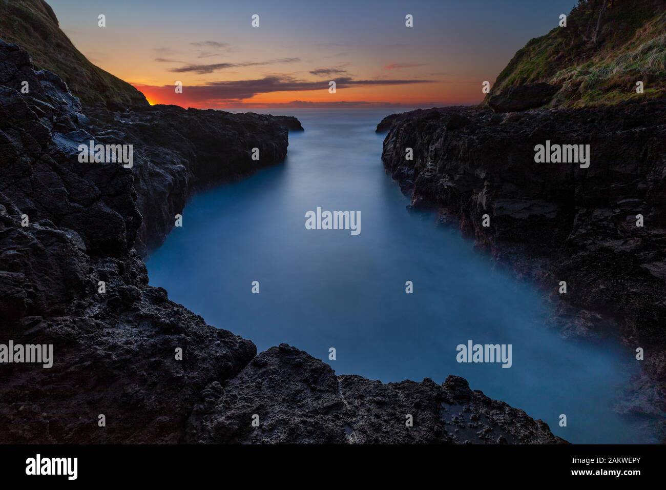 Eine lange Exposition des Wassers, das in den tiefen Einschnitt der Küste stürmt, die als Teufelsschurne in Oregon bekannt ist, während die Wintersonne untergeht. Stockfoto