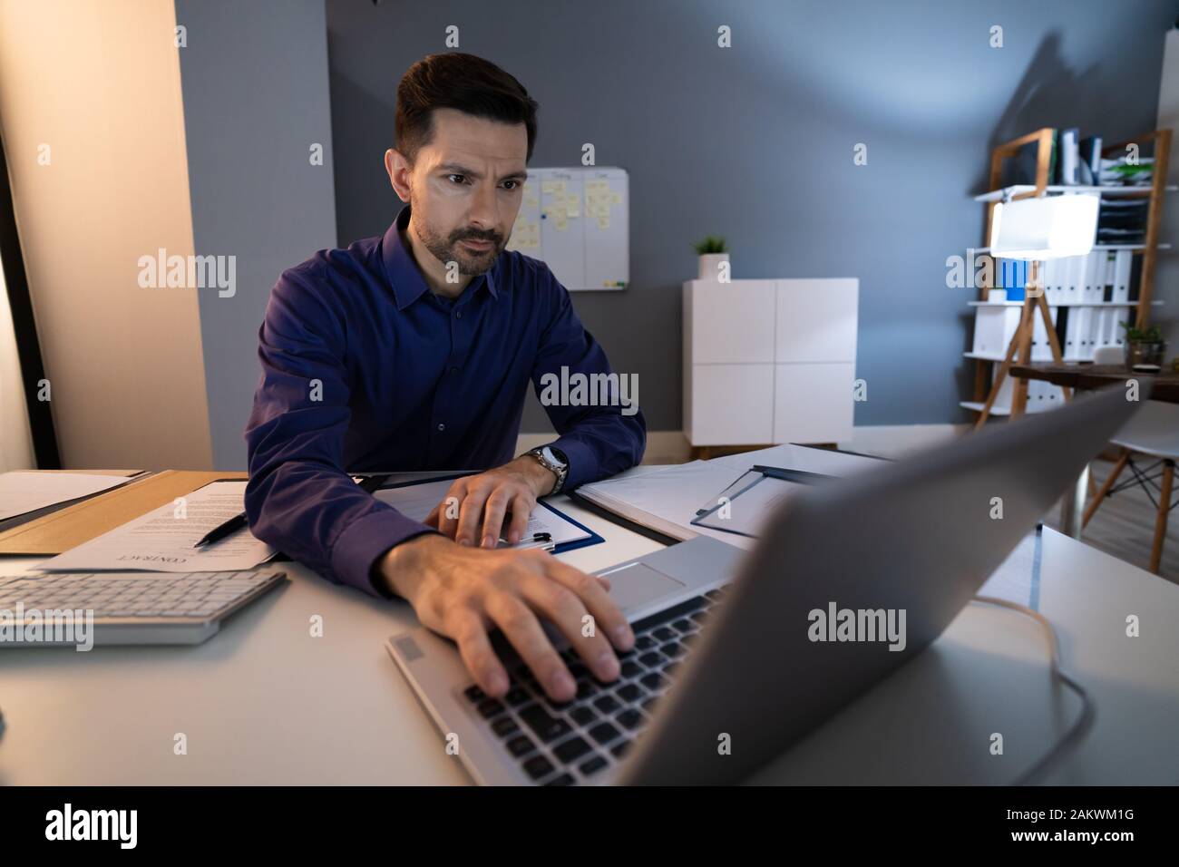 Mitte der Erwachsenen Geschäftsmanns, der spät am Schreibtisch im Büro Stockfoto