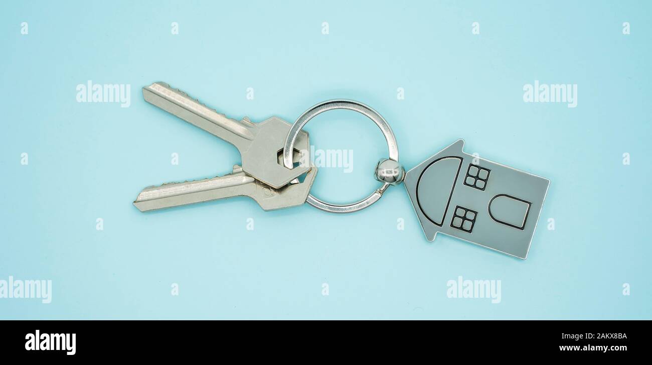 Schlüsselanhänger mit Haus Symbol und Schlüssel auf blauem Hintergrund, Immobilien Konzept Stockfoto