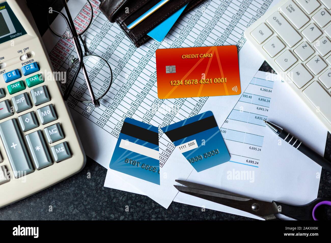 Halbieren Sie die Kreditkarte auf einem Schreibtisch mit einer Bankeinlage neben einer Computertastatur und einem Taschenrechner Stockfoto