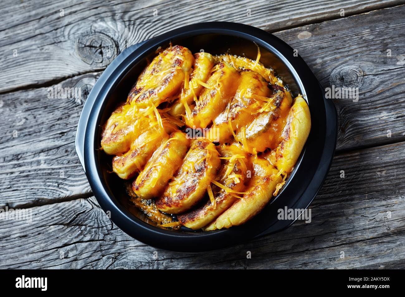 Nahaufnahme hausgemachter Kartoffelkuchen mit geriebenem Cheddar-Käse in einem schwarzen Gericht auf einem rustikalen Holztisch Stockfoto