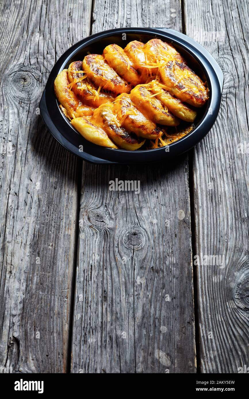 Hausgemachte Kartoffelkuchen mit geriebenem Cheddar-Käse in einem schwarzen Gericht auf einem rustikalen Holztisch, vertikaler Blick Stockfoto