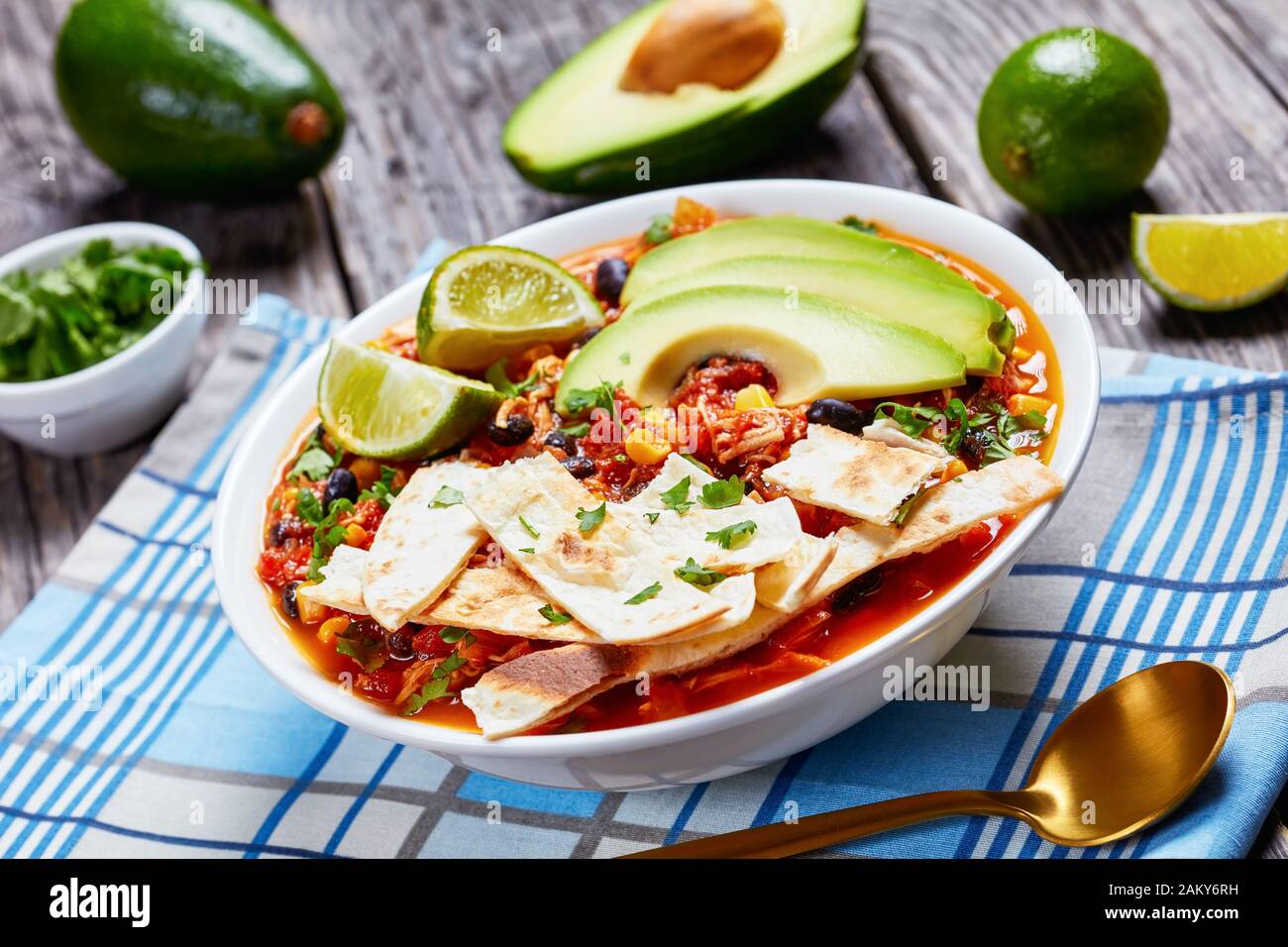 Nahaufnahme der mexikanischen zerkleinerten Chicken Taco-Suppe mit schwarzer Bohne, Maiskörnchen, mit Tortillastreifen, Avocado-Scheiben und Kalk in weißer Schüssel auf einem Stockfoto