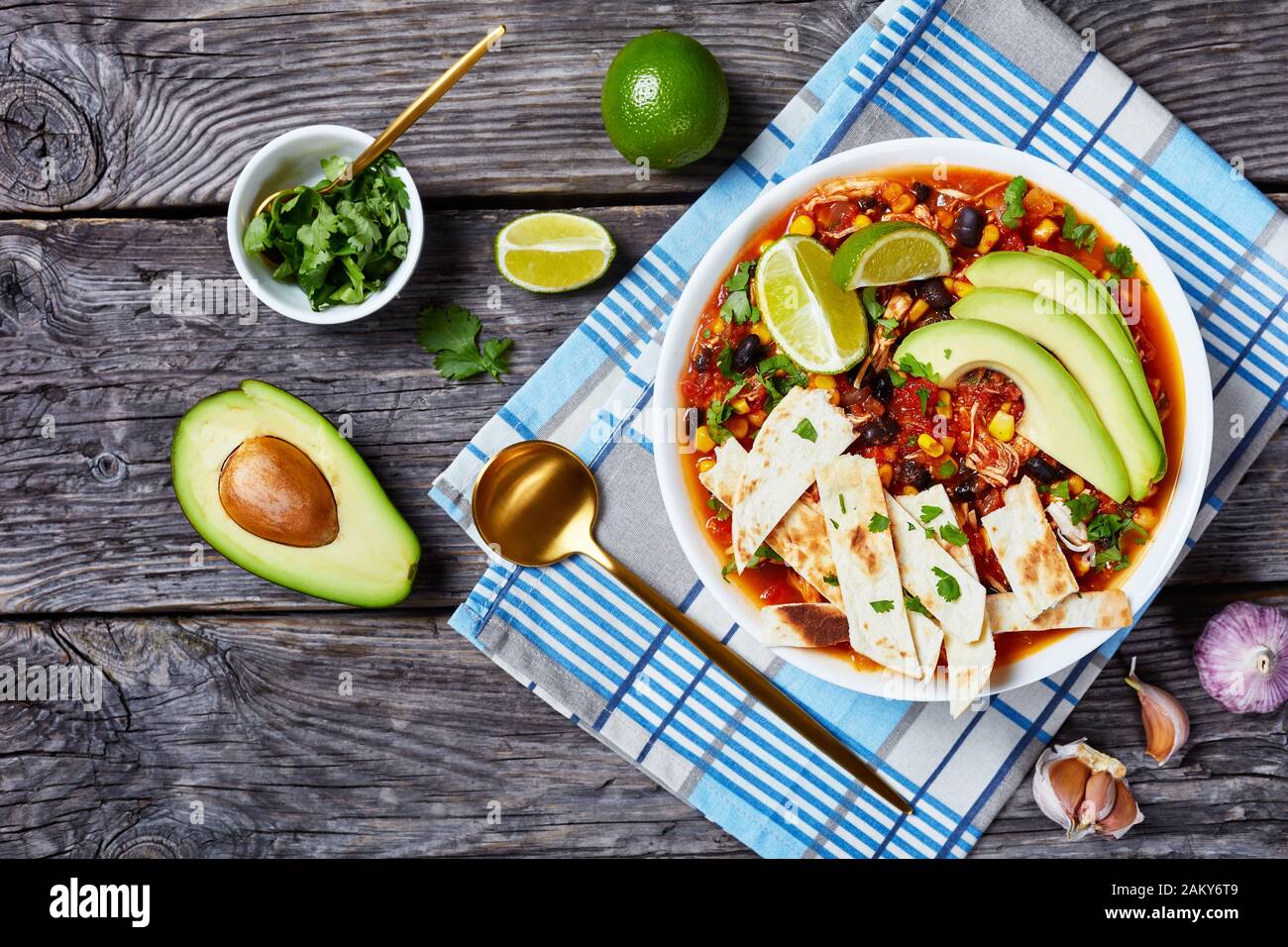 Chicken Taco Suppe mit schwarzer Bohne, Maiskörner, mit Tortillastreifen, Avocado-Scheiben und Kalk in weißer Schüssel auf einem rustikalen Holztisch, Horizont Stockfoto